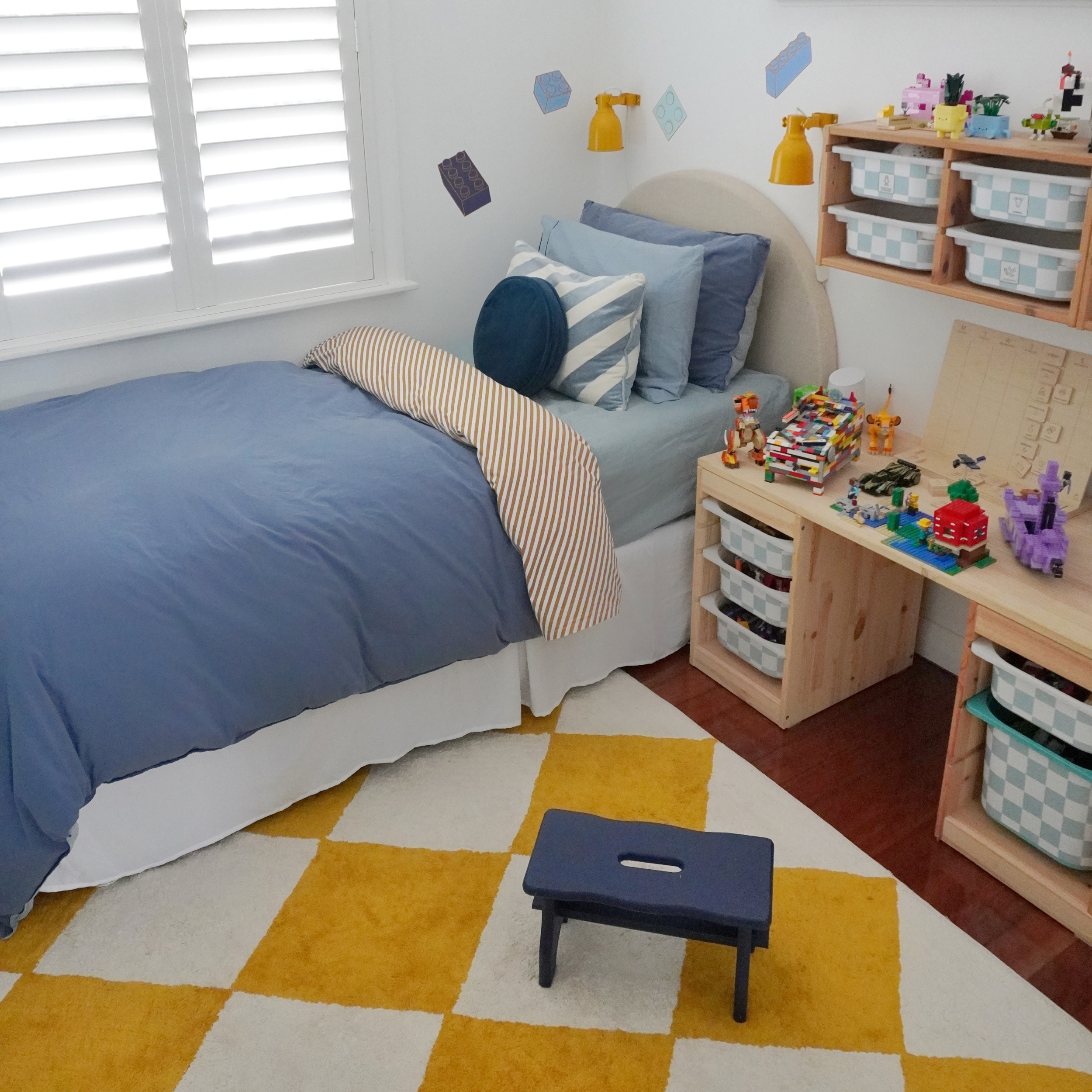 Children's bedroom with bed, desk, and toys on a checkered floor.