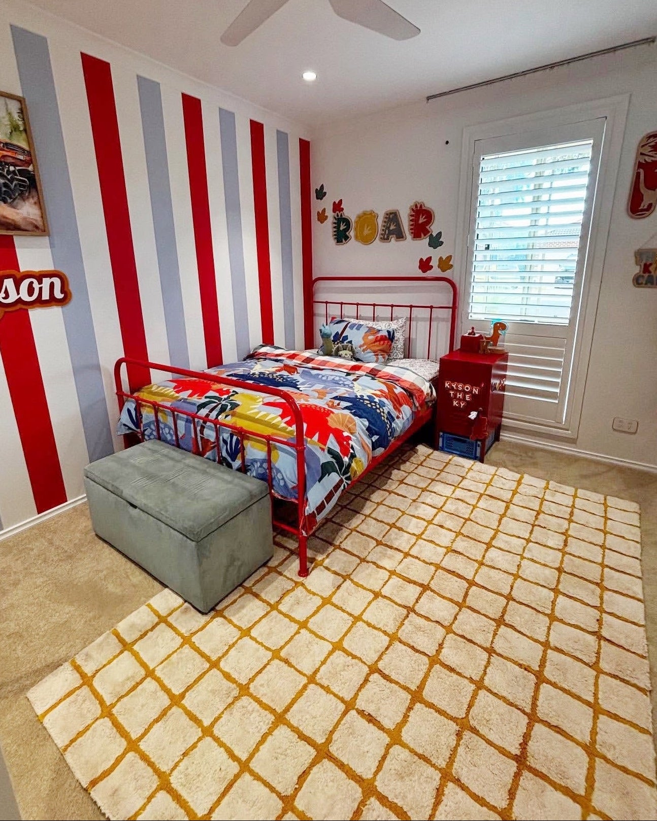 Children's bedroom with red and gray striped wall, colorful bedding, and toys.