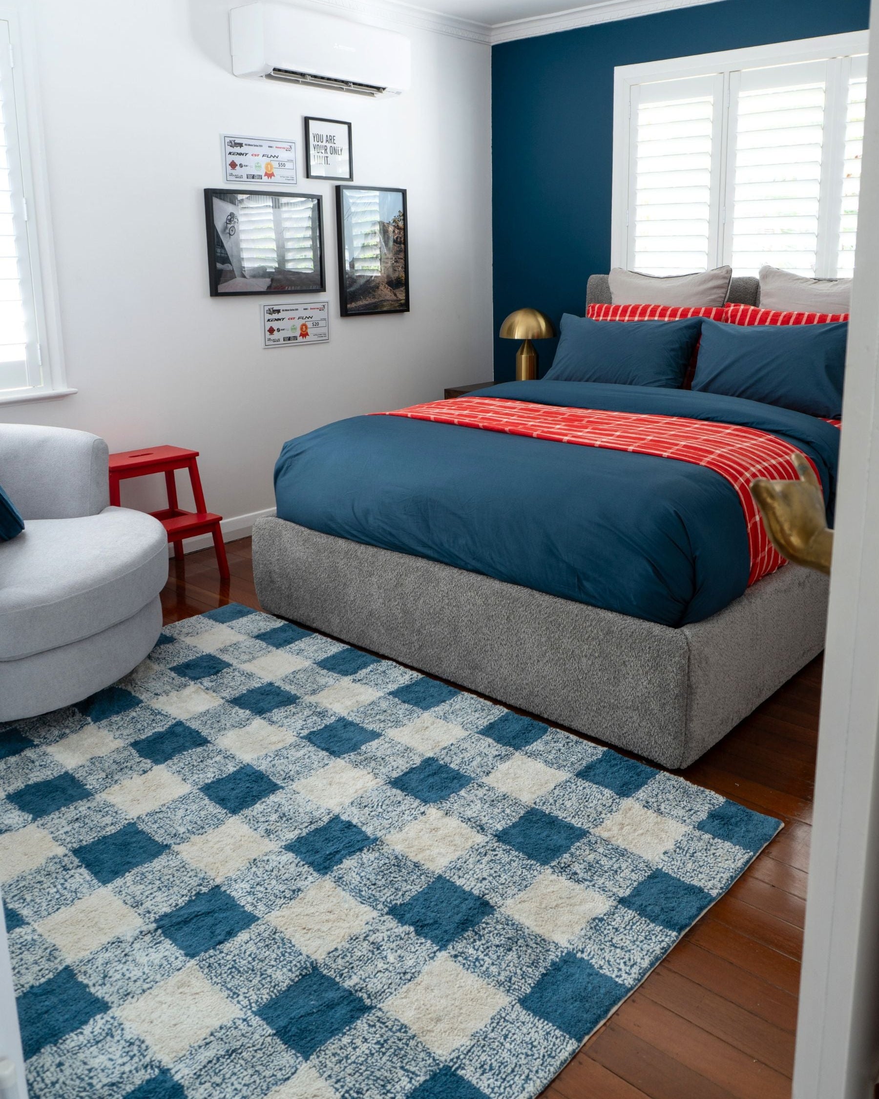 Modern bedroom with blue walls, gray bed, and checkered rug.