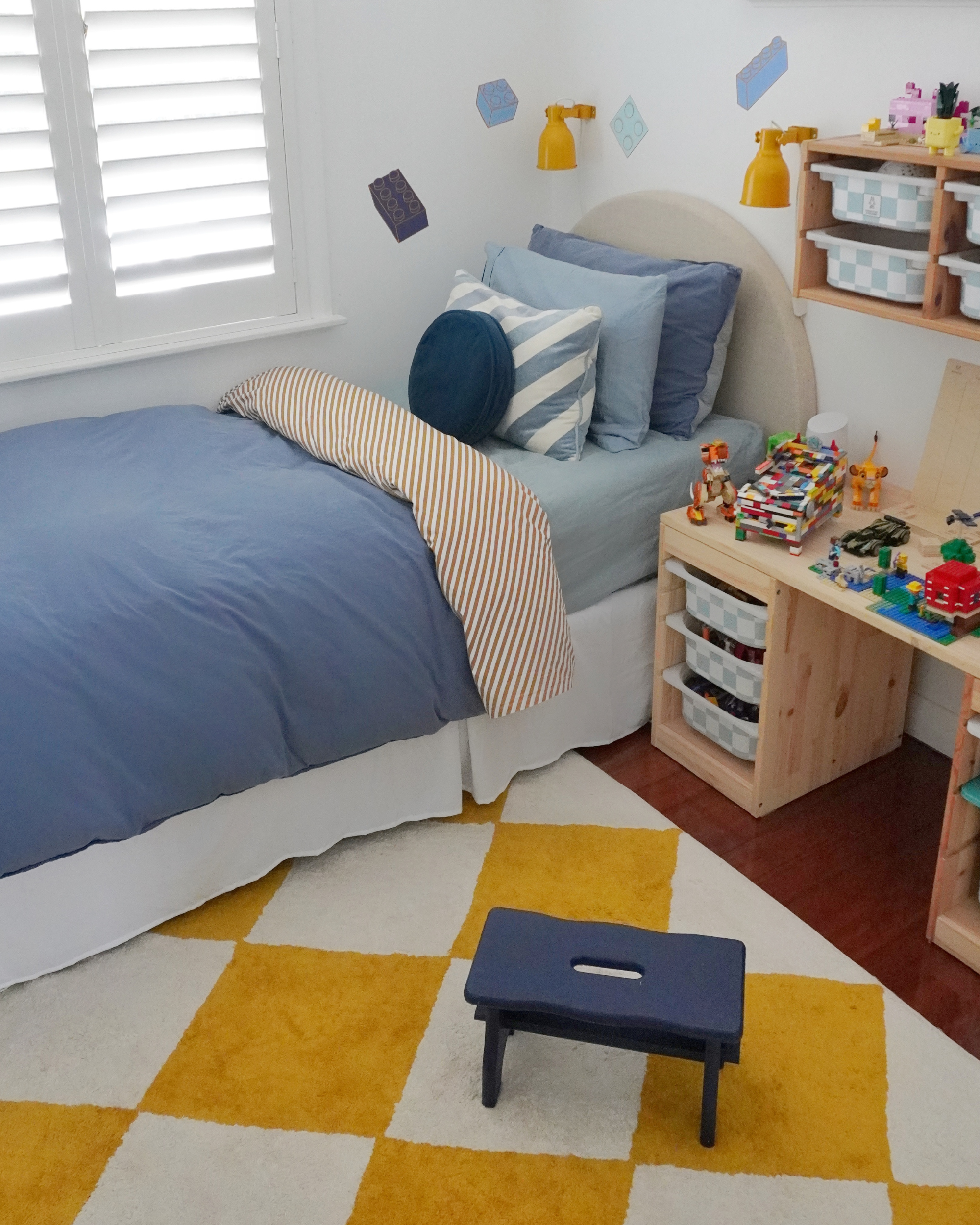 Children's bedroom with bed, desk, and toys on a checkered floor.