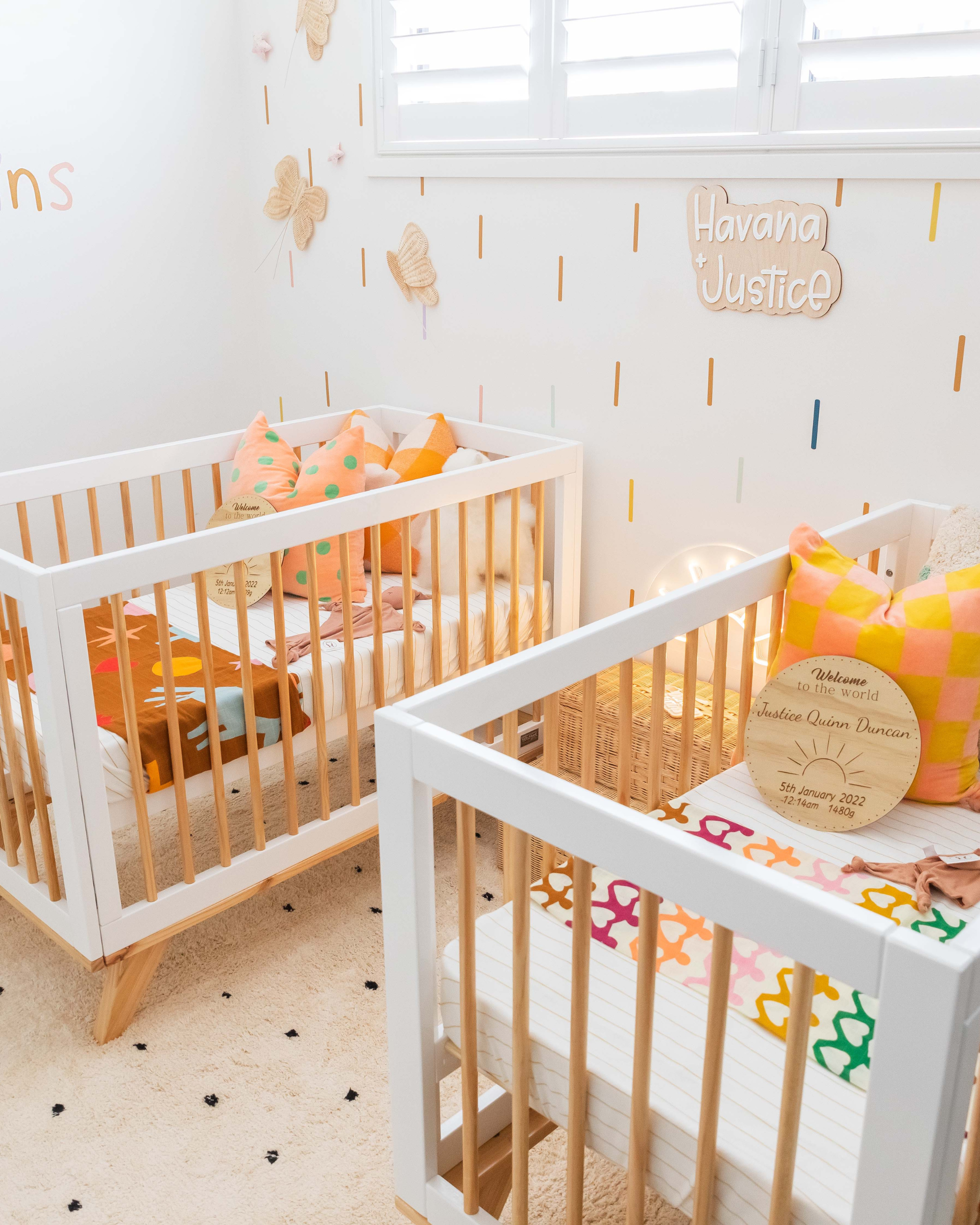Two baby cribs in a room with decorative elements and colorful accents.