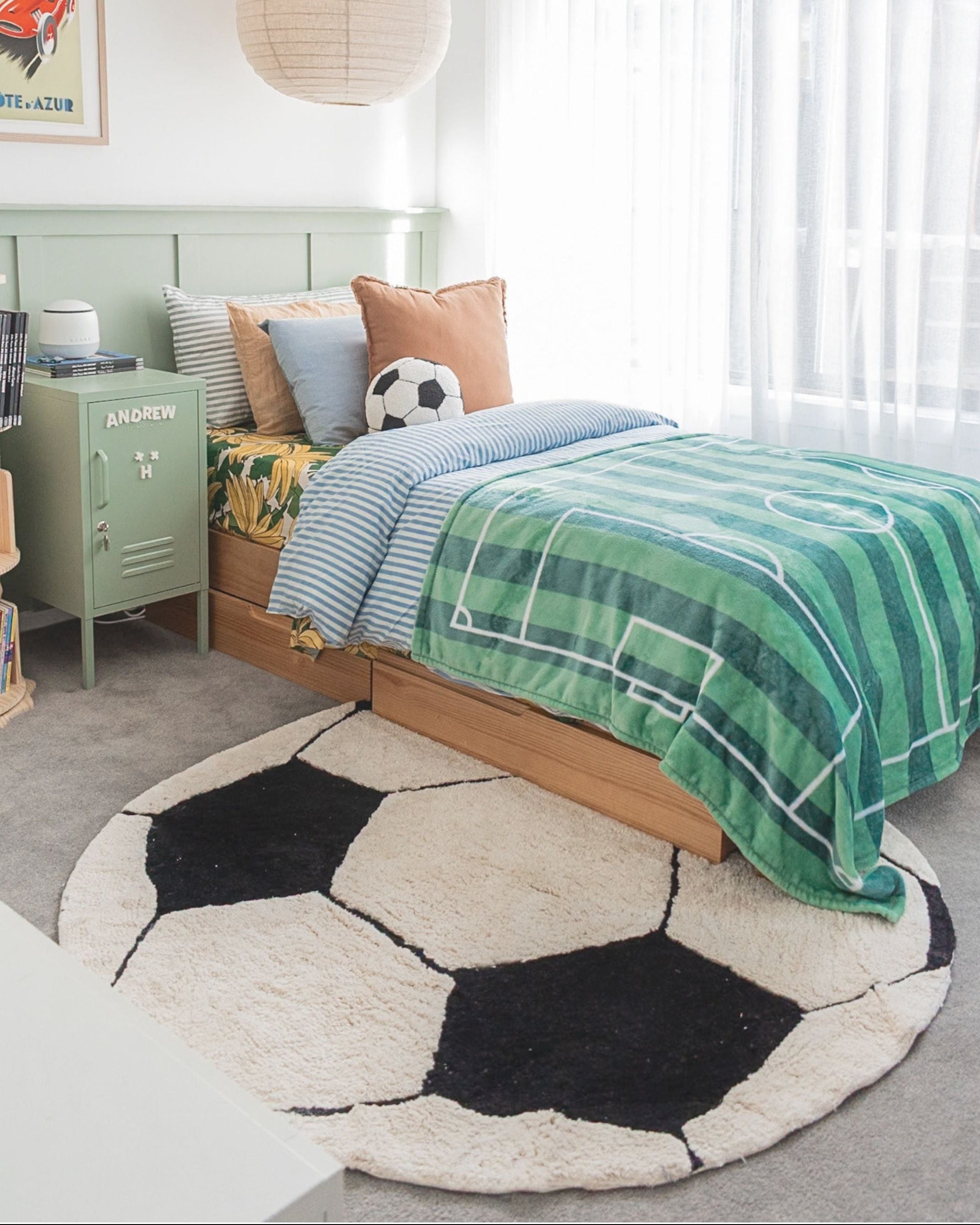 Children's bedroom with a soccer ball-shaped rug, bed with green and blue plaid blanket, and green locker.
